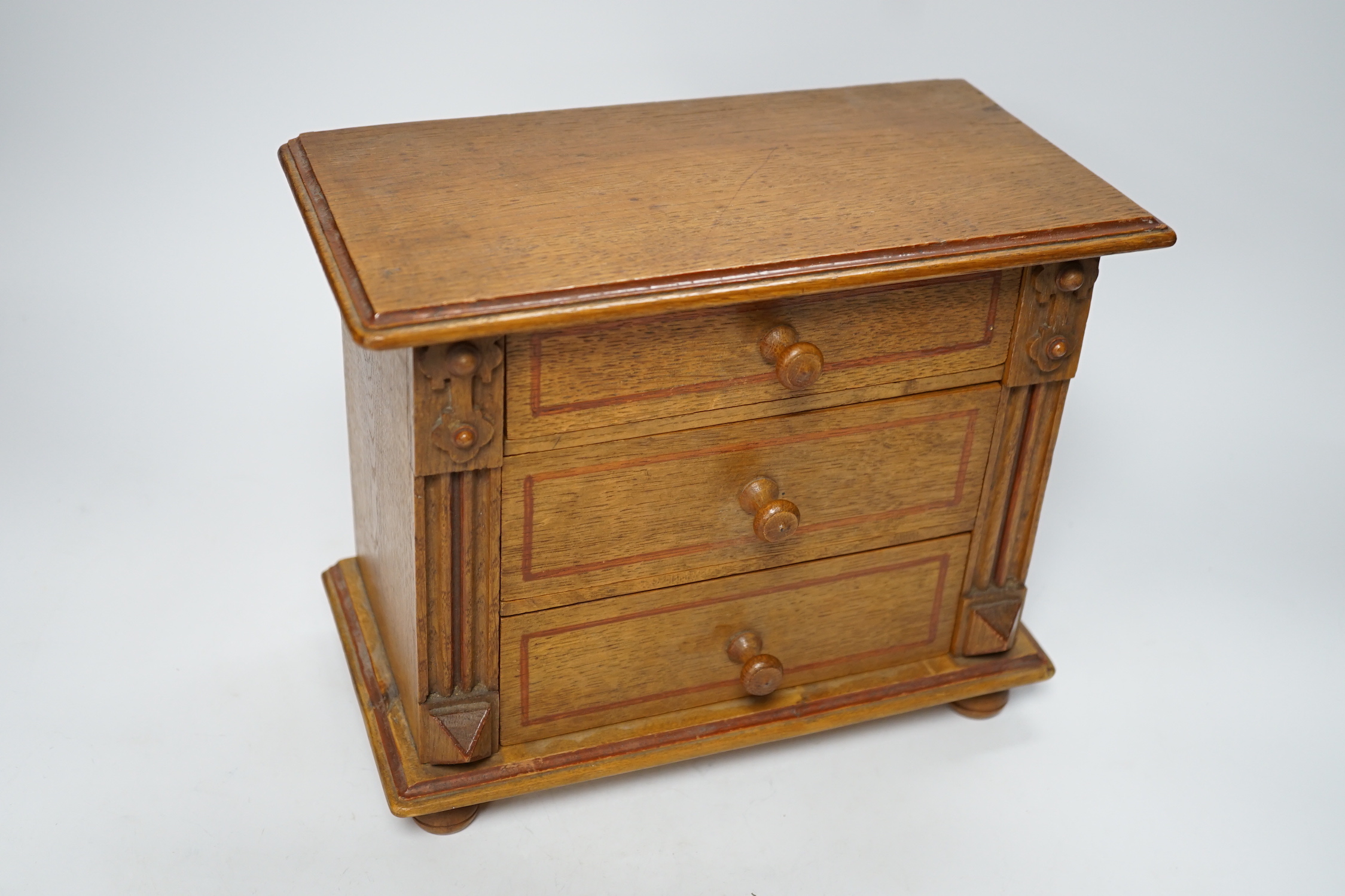 A miniature oak chest of drawers and contents (miniature bisque headed dolls and linen) height 22cm